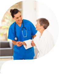 A healthcare professional in blue scrubs assists an elderly person in a white robe, providing support and care.